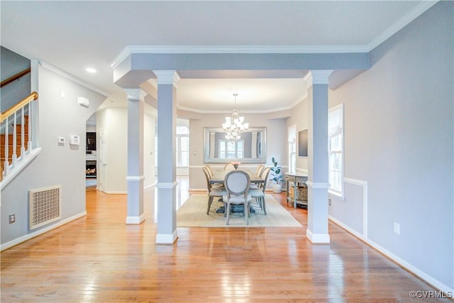 dining room with ornate columns, stairway, wood finished floors, ornamental molding, and a chandelier