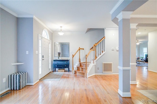 foyer entrance featuring ornate columns, stairway, light wood finished floors, ornamental molding, and baseboards