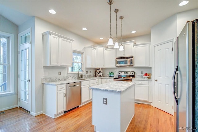 kitchen with stainless steel appliances, a sink, white cabinets, light wood finished floors, and a kitchen island