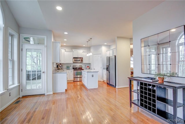 kitchen featuring stainless steel appliances, white cabinetry, light wood-style flooring, a center island, and baseboards