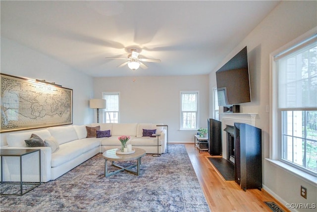 living area featuring plenty of natural light, ceiling fan, wood finished floors, and a fireplace with flush hearth