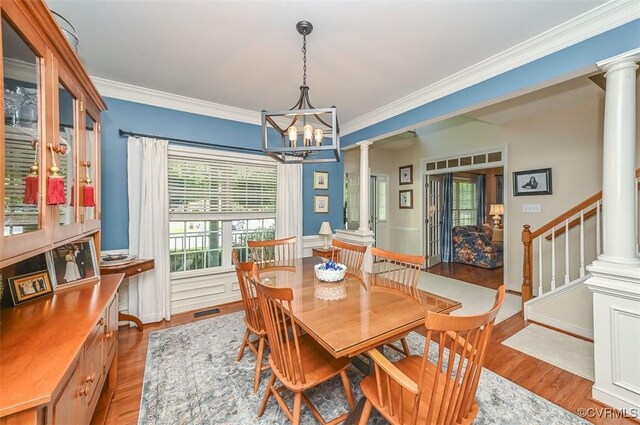 dining space with an inviting chandelier, ornamental molding, decorative columns, and wood finished floors
