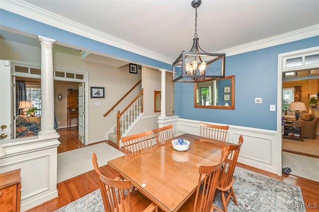 dining area featuring decorative columns, ornamental molding, wood finished floors, and stairway