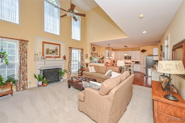 living area with plenty of natural light, a ceiling fan, a high ceiling, and a premium fireplace