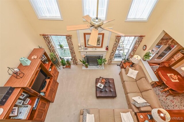 living room featuring plenty of natural light, a ceiling fan, a fireplace with flush hearth, and a high ceiling
