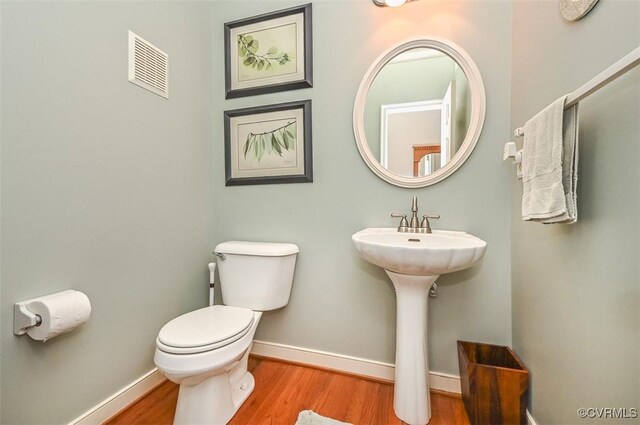 half bathroom with visible vents, baseboards, wood finished floors, and toilet