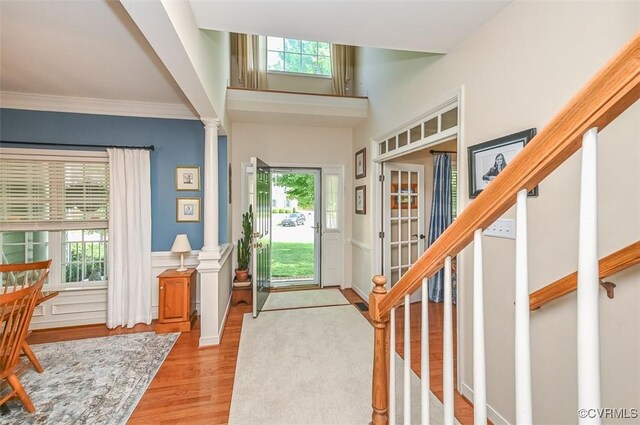 foyer entrance featuring ornamental molding, decorative columns, wainscoting, stairway, and light wood-type flooring