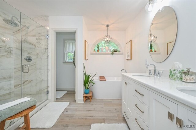 bathroom featuring double vanity, wood finished floors, a sink, a marble finish shower, and a soaking tub
