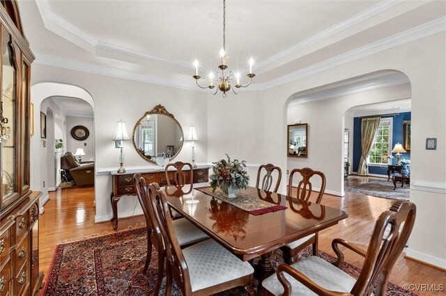 dining room featuring arched walkways, a chandelier, ornamental molding, and wood finished floors