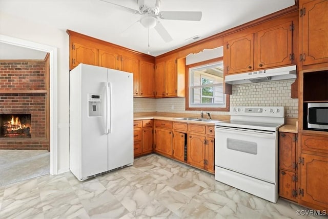 kitchen featuring brown cabinetry, light countertops, marble finish floor, under cabinet range hood, and white appliances