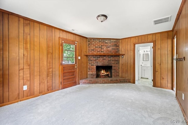 unfurnished living room with visible vents, ornamental molding, a brick fireplace, wooden walls, and carpet