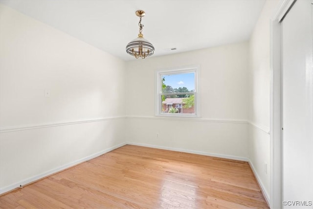 empty room featuring light wood-type flooring, baseboards, a notable chandelier, and visible vents