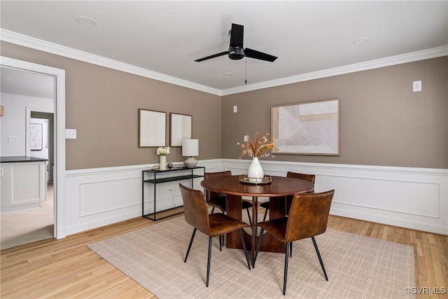 dining space featuring light wood-style floors, crown molding, ceiling fan, and a wainscoted wall