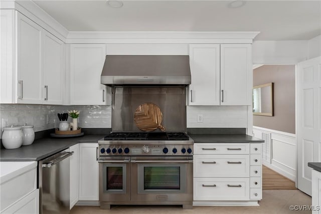 kitchen with dark countertops, extractor fan, stainless steel appliances, white cabinetry, and tasteful backsplash