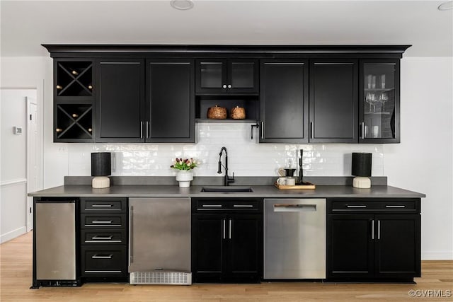 bar with backsplash, appliances with stainless steel finishes, a sink, baseboards, and light wood-style floors