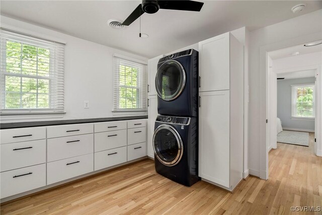 clothes washing area with ceiling fan, baseboards, stacked washer / dryer, light wood-type flooring, and visible vents