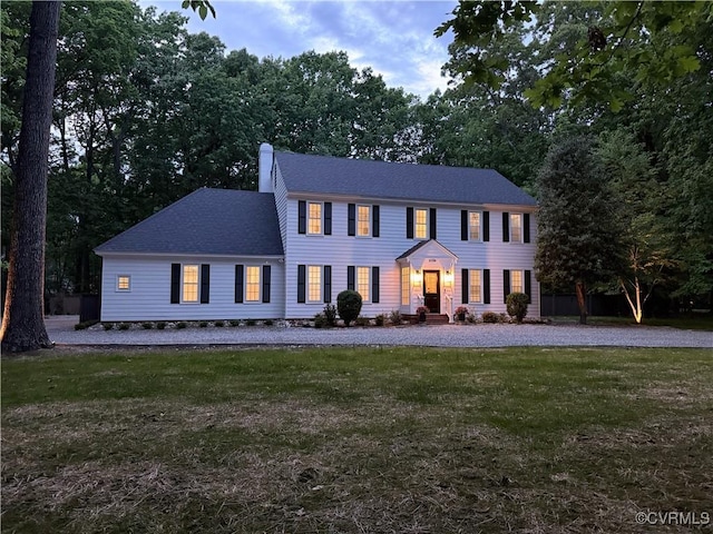 colonial-style house featuring a shingled roof, a front yard, and a chimney