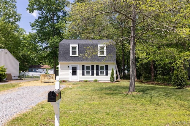 colonial inspired home featuring a front lawn, fence, gravel driveway, a gambrel roof, and a shingled roof