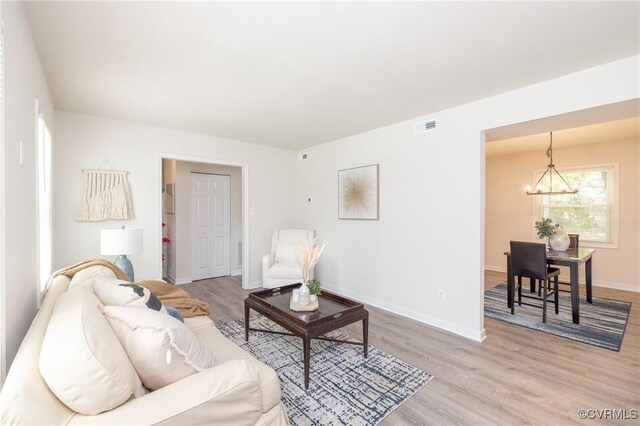 living room featuring a notable chandelier, visible vents, baseboards, and light wood-style floors