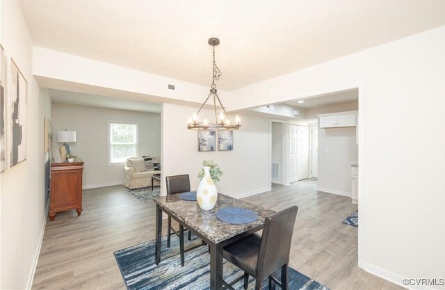 dining area featuring baseboards, a notable chandelier, light wood-style flooring, and visible vents