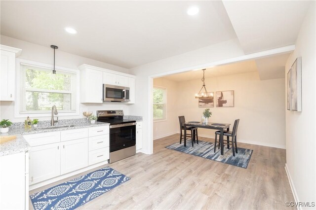 kitchen with appliances with stainless steel finishes, white cabinetry, a sink, light stone counters, and light wood-style flooring