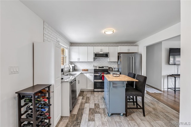 kitchen with a breakfast bar area, appliances with stainless steel finishes, a sink, white cabinets, and butcher block counters