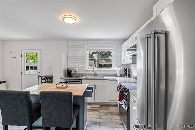 kitchen with a breakfast bar area, tasteful backsplash, a sink, wood counters, and stainless steel appliances