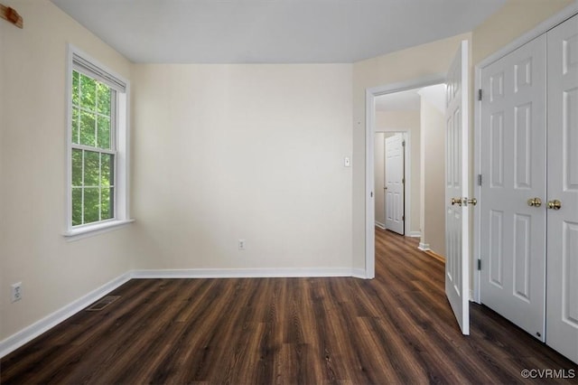 unfurnished bedroom with baseboards, a closet, dark wood-style floors, and visible vents