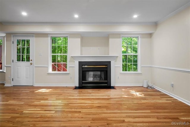 unfurnished living room featuring crown molding, baseboards, wood finished floors, and a wealth of natural light