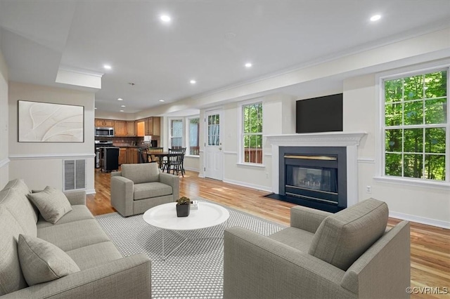 living room featuring visible vents, a fireplace with flush hearth, light wood-style flooring, and plenty of natural light
