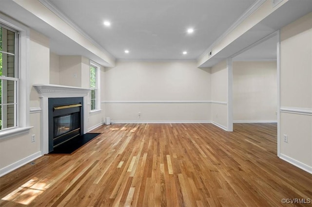 unfurnished living room featuring baseboards, a glass covered fireplace, ornamental molding, and wood finished floors