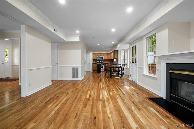living area featuring light wood-style floors, visible vents, a glass covered fireplace, ornamental molding, and recessed lighting