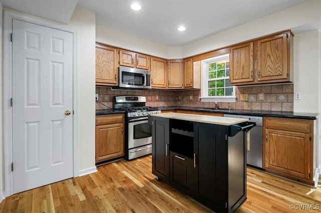 kitchen featuring dark countertops, appliances with stainless steel finishes, a sink, light wood-style flooring, and recessed lighting