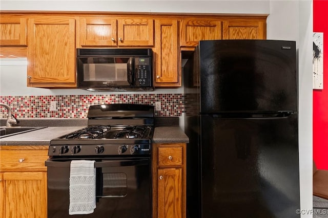 kitchen with dark countertops, brown cabinets, a sink, backsplash, and black appliances