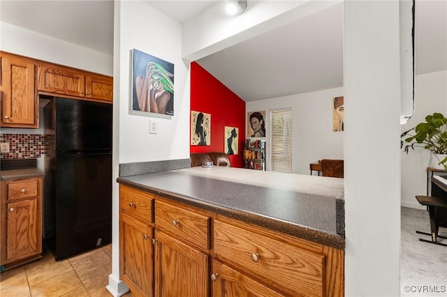 kitchen featuring freestanding refrigerator, decorative backsplash, lofted ceiling, dark countertops, and brown cabinets