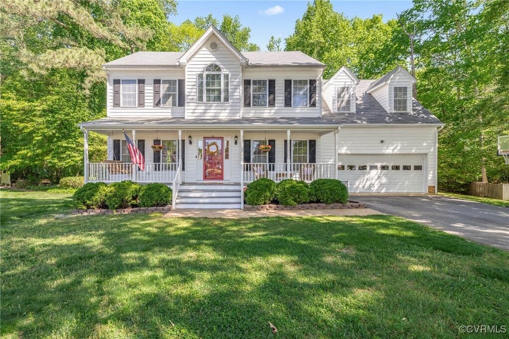 colonial inspired home with covered porch, an attached garage, a front yard, and aphalt driveway