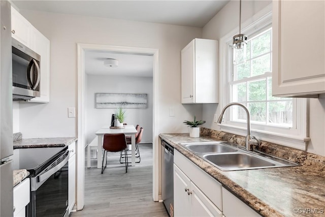 kitchen with pendant lighting, white cabinets, a sink, light wood-style flooring, and appliances with stainless steel finishes