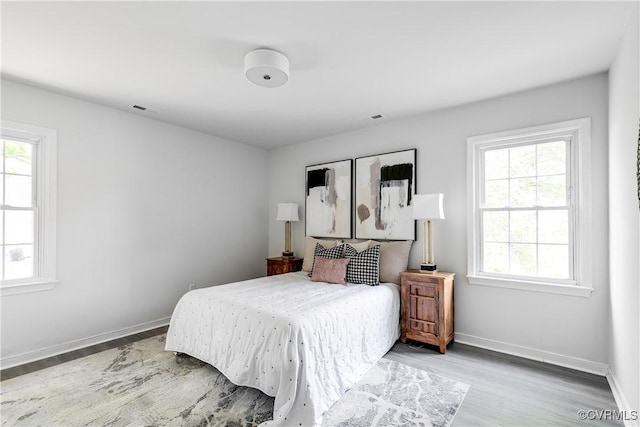 bedroom with baseboards, visible vents, multiple windows, and wood finished floors