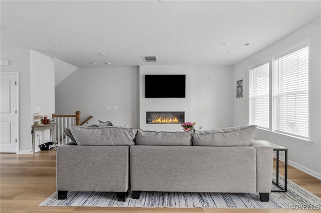 living room with baseboards, visible vents, a glass covered fireplace, and light wood-style floors
