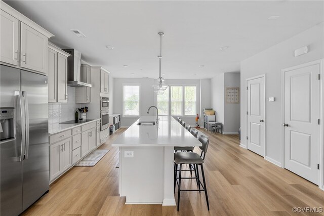 kitchen featuring a sink, appliances with stainless steel finishes, light wood-style flooring, and wall chimney exhaust hood