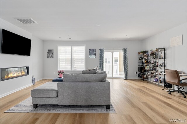 living area with a glass covered fireplace, baseboards, light wood-style flooring, and visible vents