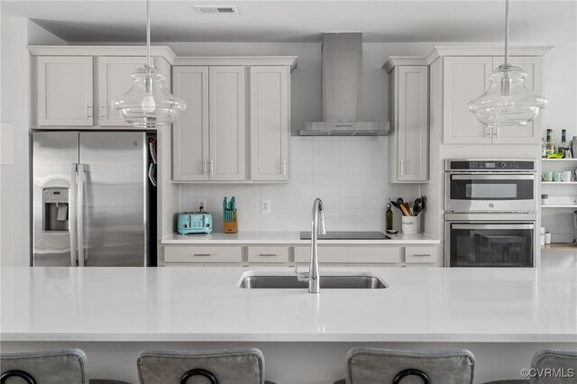 kitchen with wall chimney range hood, stainless steel appliances, a sink, and a kitchen bar