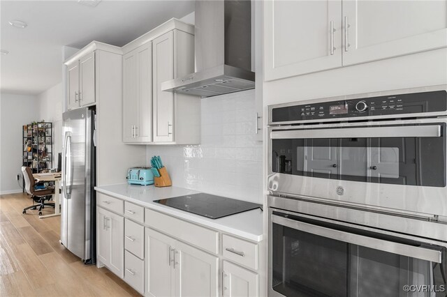 kitchen featuring light wood-style floors, wall chimney exhaust hood, white cabinetry, appliances with stainless steel finishes, and backsplash