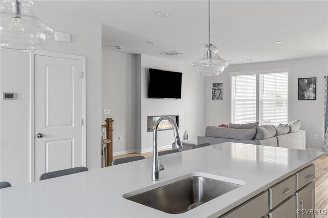 kitchen with pendant lighting, wood finished floors, open floor plan, light countertops, and a sink