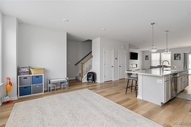 kitchen featuring open floor plan, an island with sink, light wood-type flooring, a sink, and dishwasher