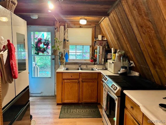 kitchen with stainless steel electric range, a sink, light countertops, brown cabinetry, and light wood-type flooring