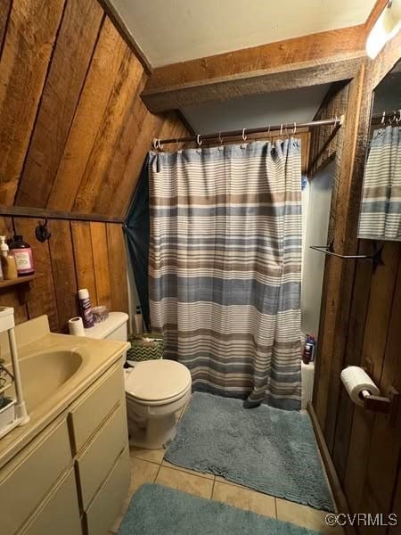 bathroom with tile patterned flooring, vanity, toilet, wood walls, and vaulted ceiling