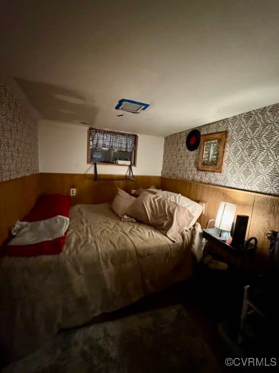 bedroom featuring wooden walls, wainscoting, and wallpapered walls