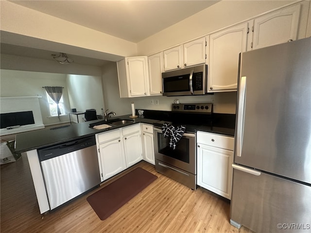 kitchen with a sink, appliances with stainless steel finishes, white cabinets, dark countertops, and light wood-style floors
