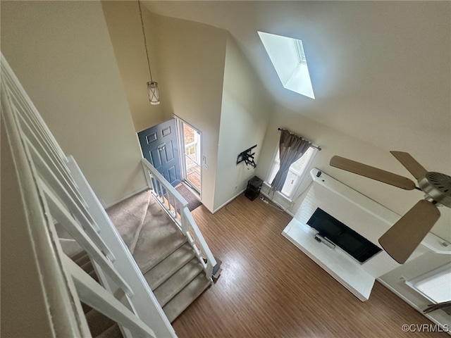 living area with wood finished floors, a fireplace, a skylight, baseboards, and a towering ceiling